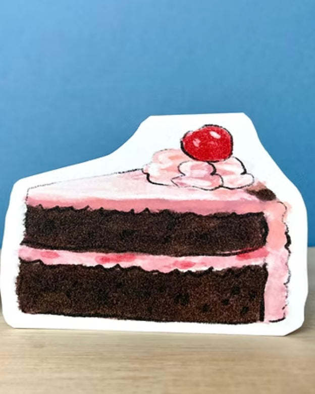 Greeting card shaped like a slice of cake with pink frosting and a cherry on top against a blue background.