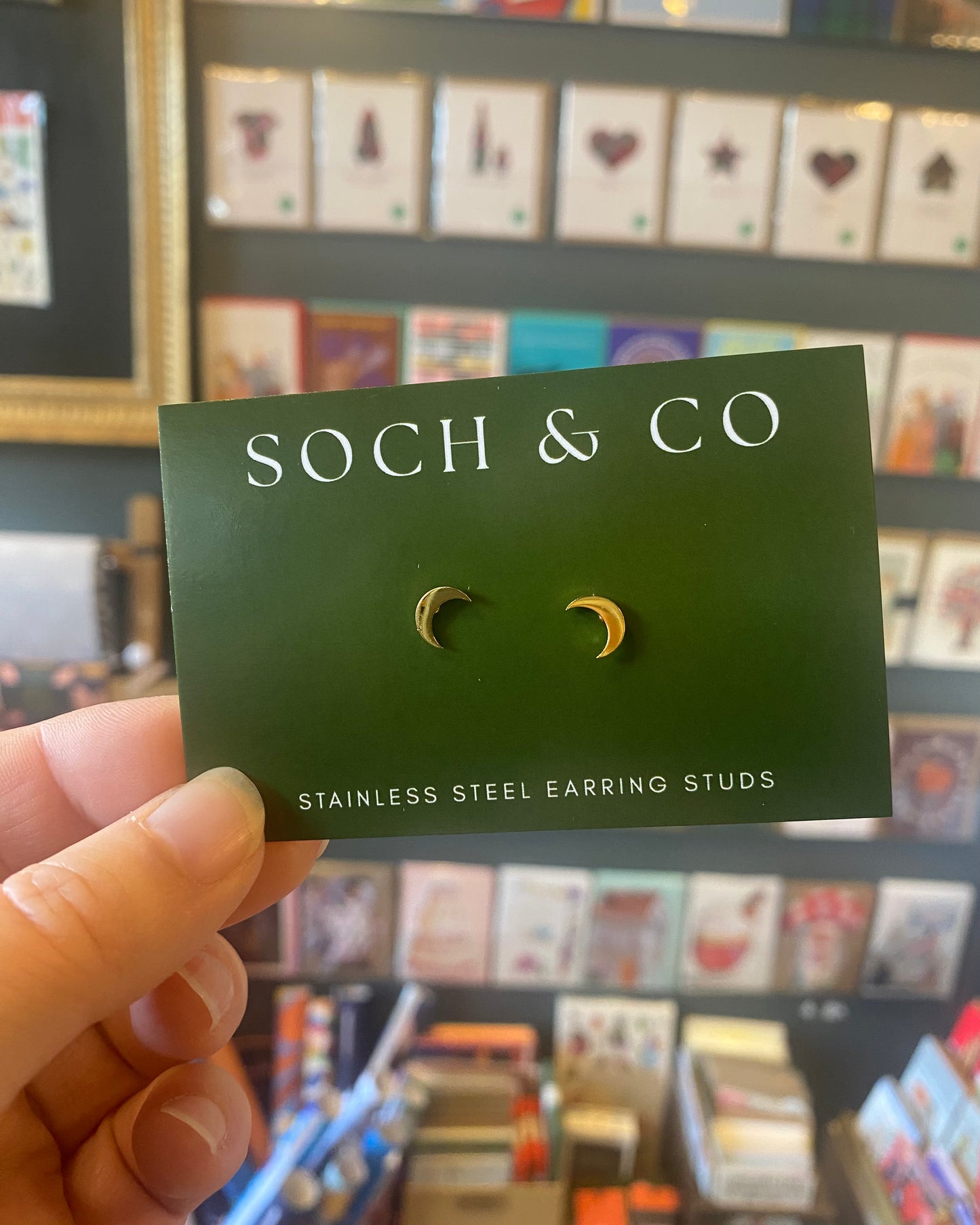 Moon shapedarring card with 'SOCH & CO' branding held by a hand in front of a store display.