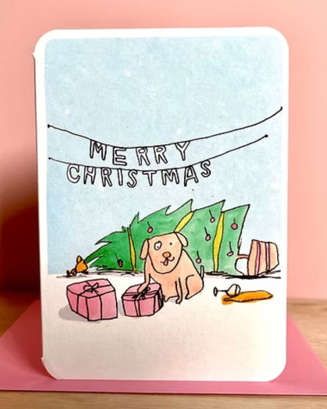 Card with a dog and fallen Christmas tree illustration and 'Merry Christmas' text on a pink envelope.