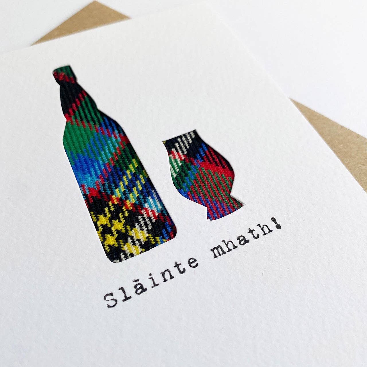 Colourful tartan bottle and glass shapes on a card with 'Sláinte mhaith!' text on a white background
