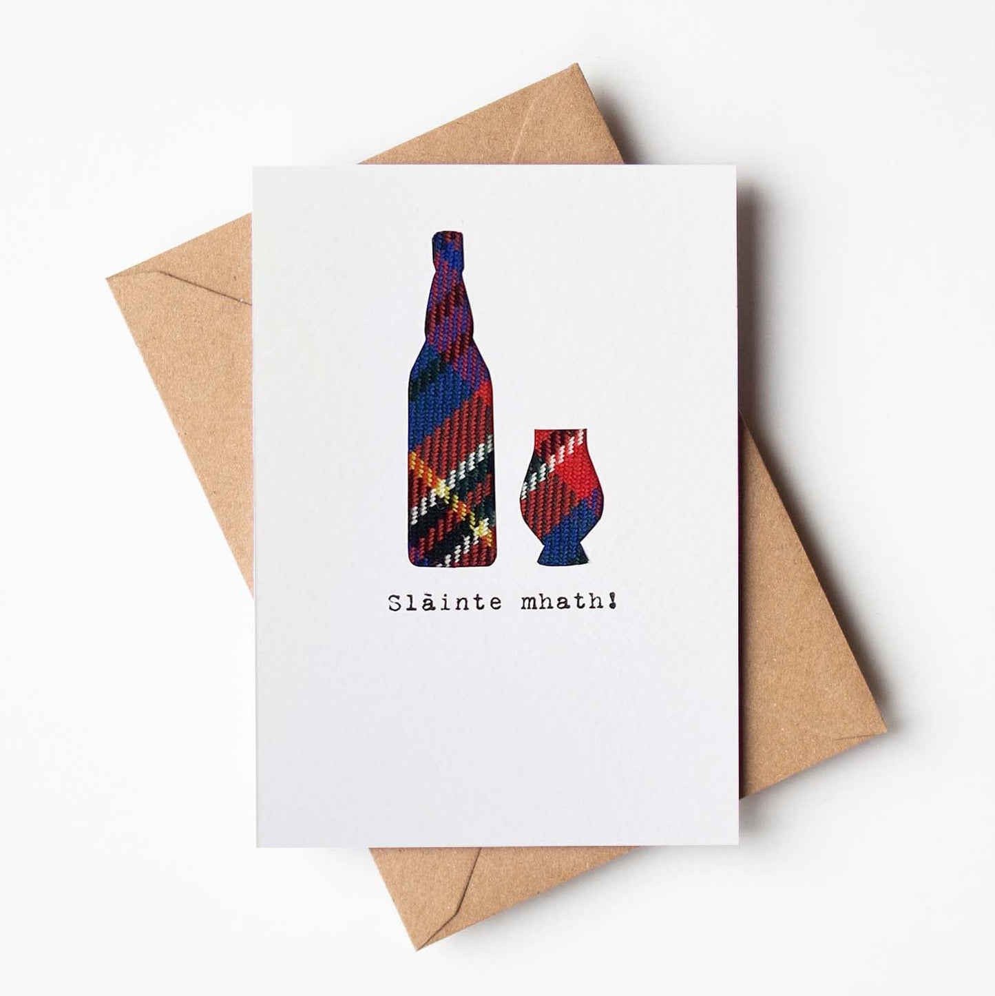 Greeting card with tartan bottle and glass design and 'Sláinte mhaith!' text, featuring a brown envelope.
