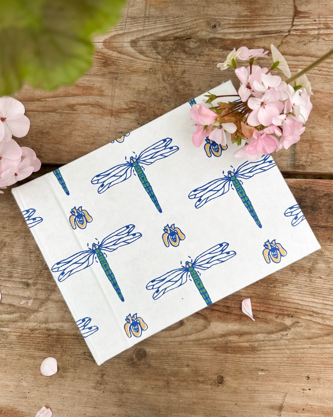 White photo album with blue dragonfly pattern on a wooden surface with flowers.