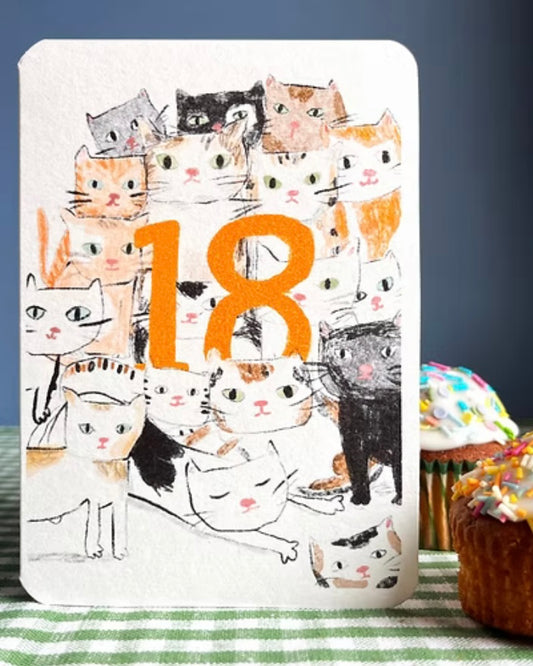 Greeting card with cat illustrations and the number 18 on a table with cupcakes.