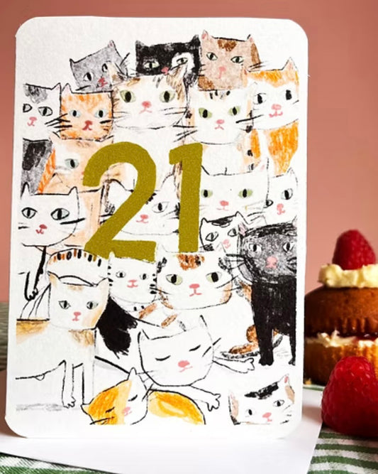 Card with cat illustrations and the number 21, placed on a surface with a cake and strawberries.
