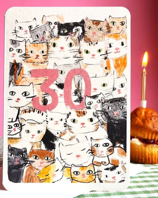 Card with cat illustrations and the number 30, next to a birthday cake with a candle.