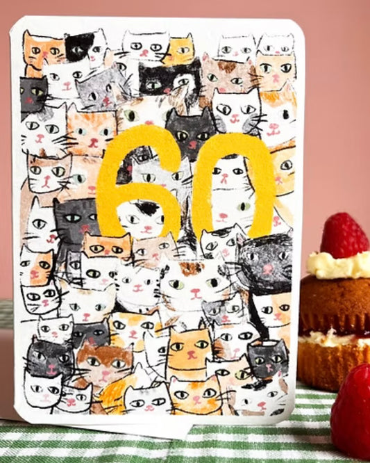 Card with cat pattern and yellow number 60 on a checkered tablecloth with cake and strawberries.