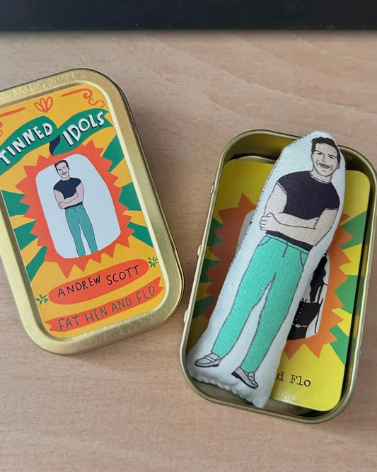 Small plush toy of Andrew Scott in a tin with 'Tinned Idols' label on a wooden surface