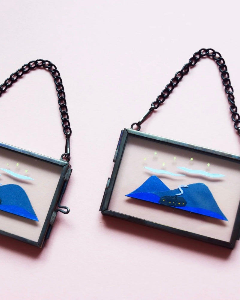 Two framed mini glass frames with blue mountain and both designs on a pink background