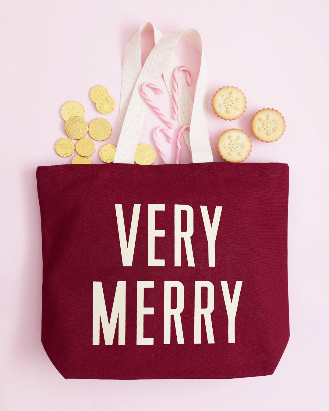 Red tote bag with 'Very Merry' text, on a pink background