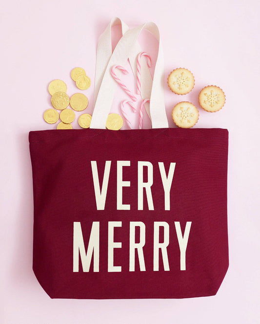 Red tote bag with 'Very Merry' text, on a pink background