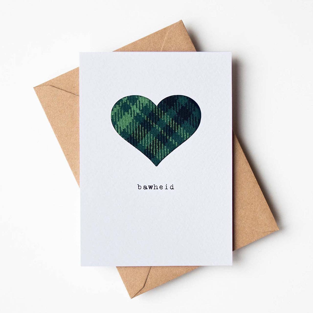 Card with a real green cloth tartan heart and 'bawheld' text, accompanied by a brown envelope on a white background.