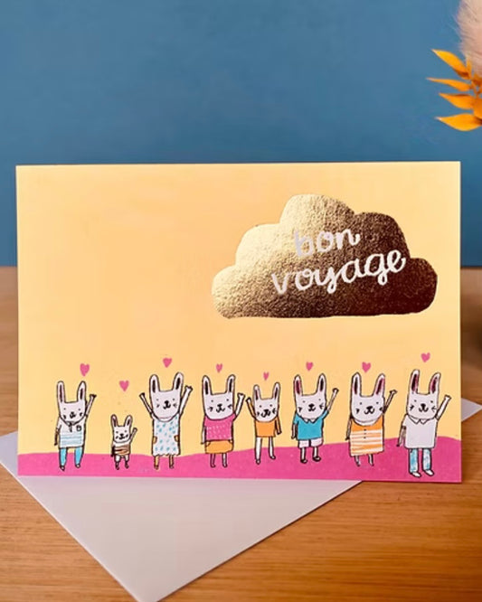 Greeting card with gold foil cloud containing the text ‘Bon Voyage’ and cartoon bunnies waving goodbye, on an envelope