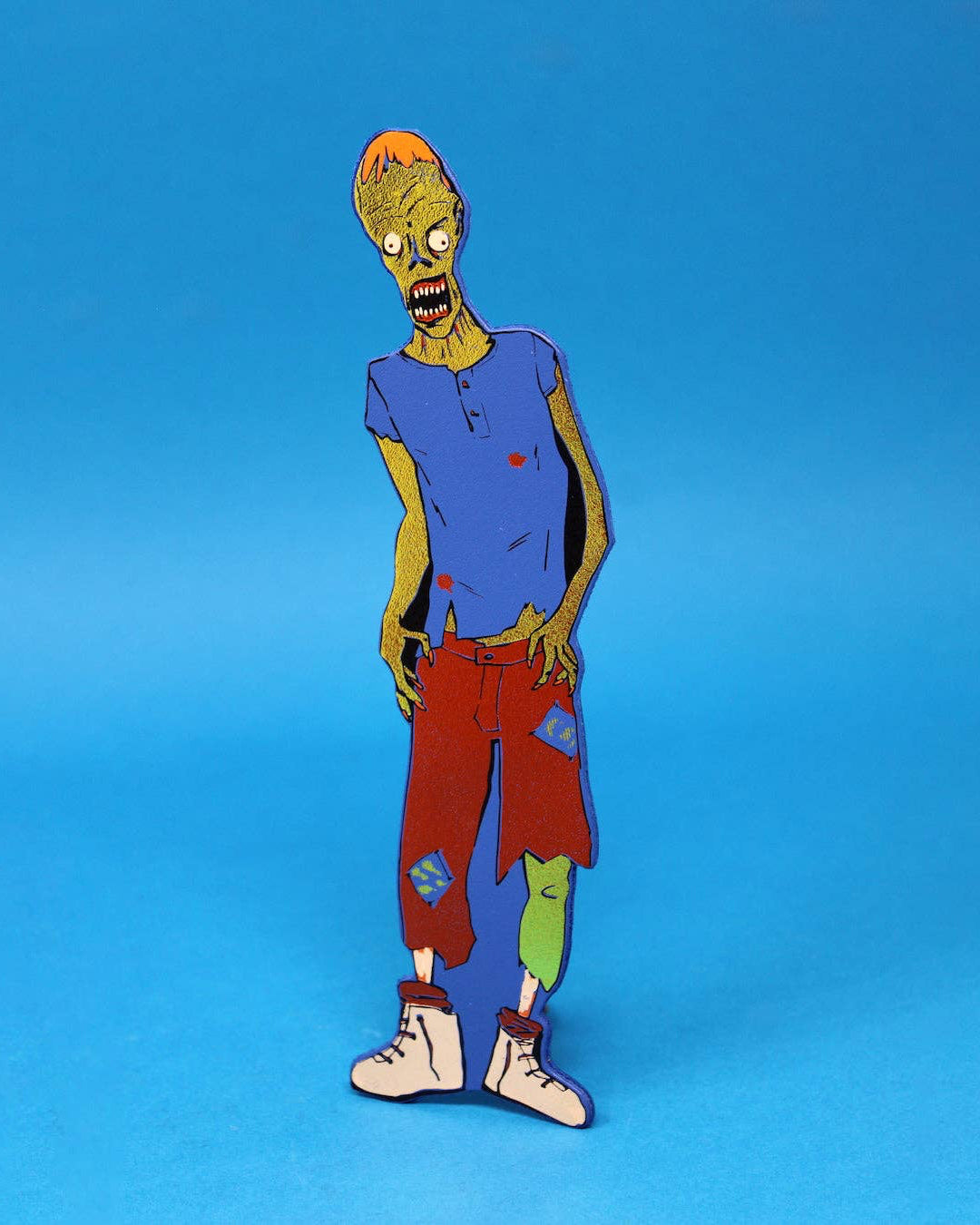 A leather bookmark shapes like a zombie character, standing upright against a solid blue background.