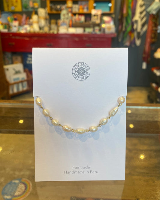 Pearl bracelet on a white card with 'Fair Trade' and 'Handmade in Peru' text, displayed against a blurred store background.