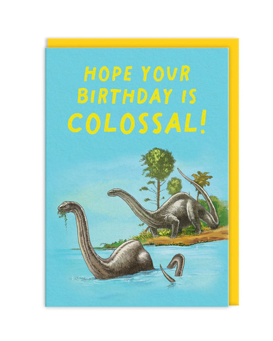 Birthday card with dinosaurs and text 'Hope your birthday is colossal!' on a blue background, other a yellow envelope,.
