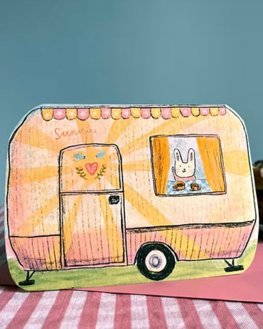 Caravan shaped card with a bunny character inside, sitting on an envelope,  on a checkered surface