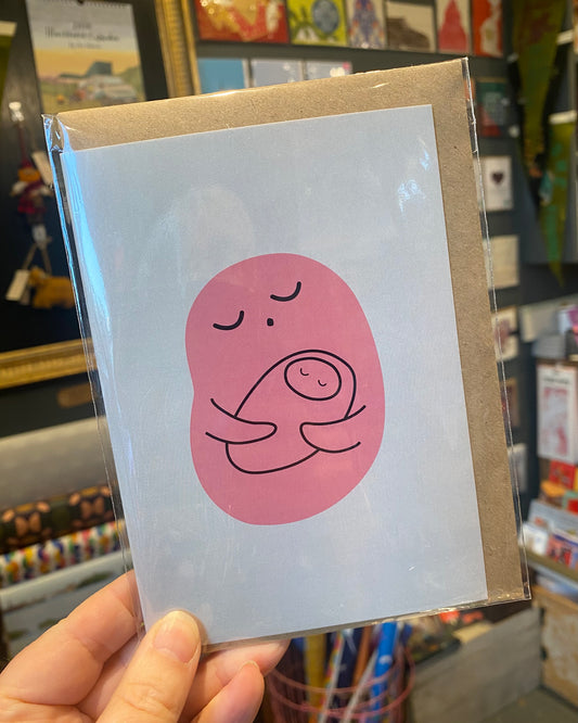 Card with a pink abstract baby design held in front of a store shelf.