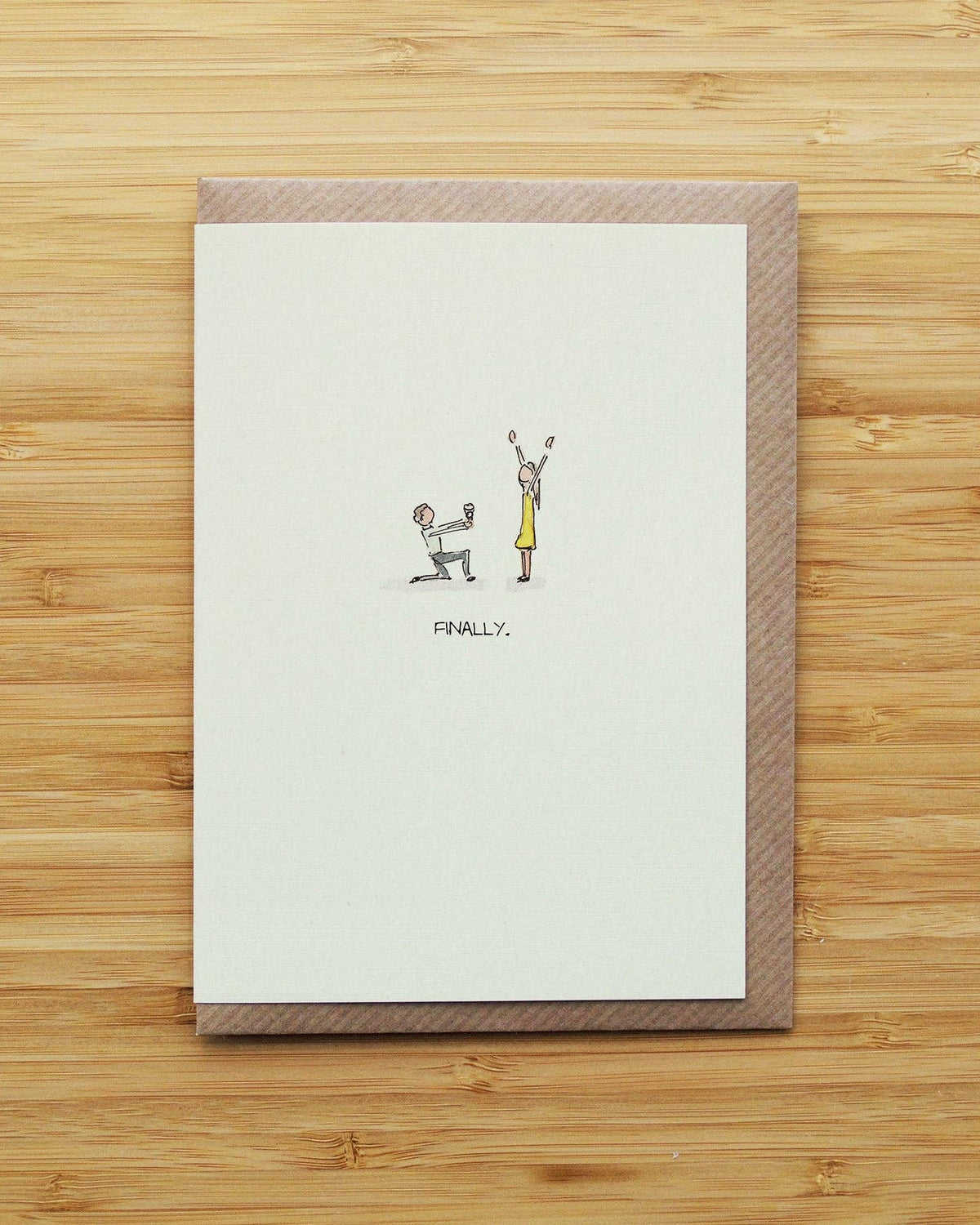 Engagement greeting card with illustrations of two people and the word 'FINALLY' on a wooden surface