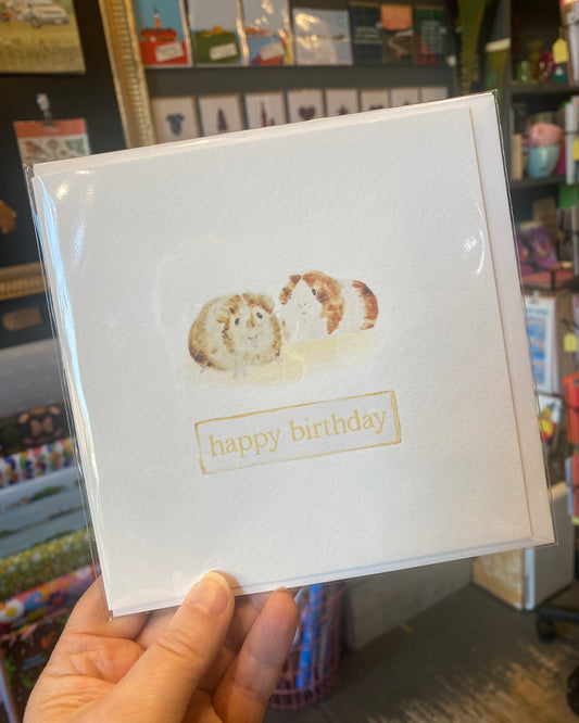Handheld birthday card with guinea pig illustration in a store setting