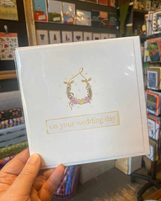 White card with horseshoe illustration and gold text 'on your wedding day' held in front of a store display.