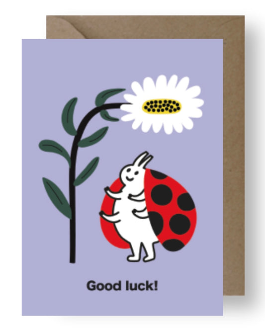 Greeting card with a cartoon ladybug and flower and the words ‘Good Luck’ on a purple background.