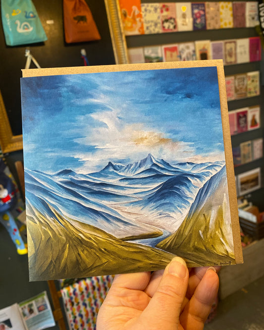 Handheld card with a mountain landscape painting in front of a colorful background.