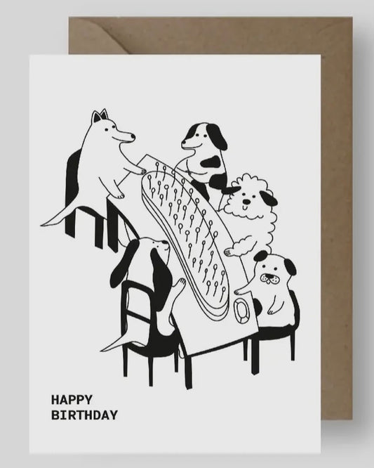 Greeting card with black and white illustration of dogs at a table and 'Happy Birthday' text, with a brown envelope