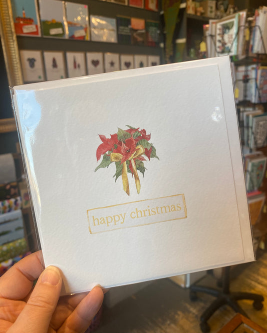 White card with poinsettia design and 'happy christmas' text held in a hand.