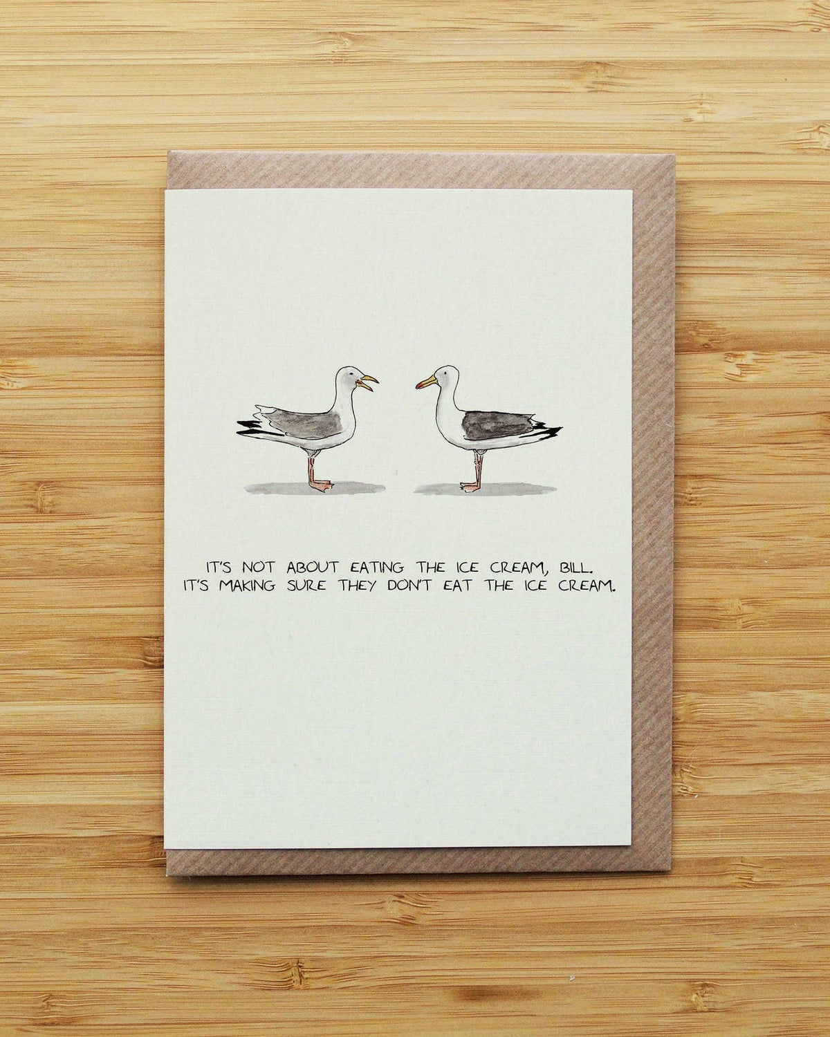 A greeting card with a brown envelope, featuring an illustration of two seagulls facing each other with the handwritten text: 'IT'S NOT ABOUT EATING THE ICE CREAM, BILL. IT'S MAKING SURE THEY DON'T EAT THE ICE CREAM.