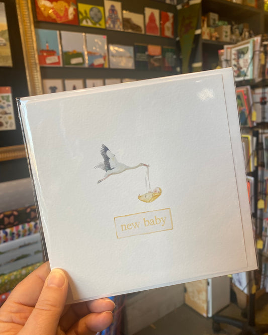 Card with a stork and baby illustration held in front of a bookshelf.