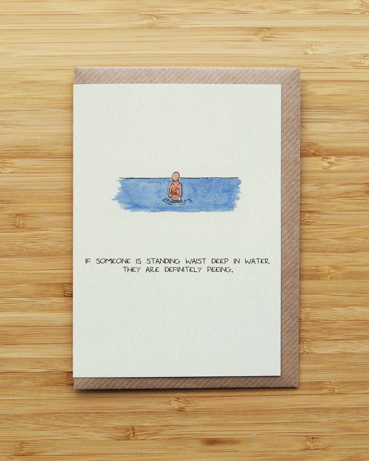 Card with a humorous illustration of a person standing in water and text, on a wooden surface.