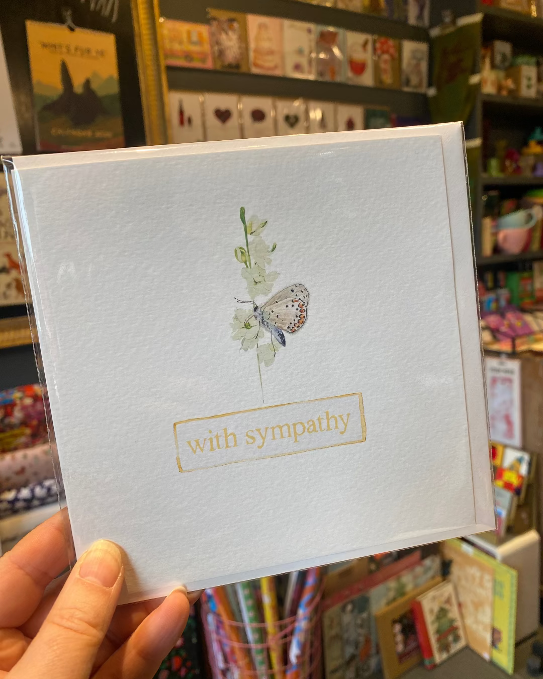 Card with 'with sympathy' text held in a hand with a bookshelf background