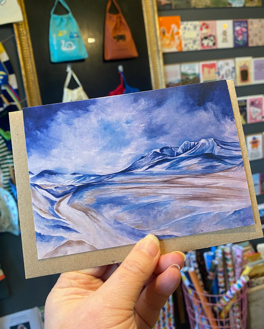 Hand holding a small landscape painting with blue and brown tones.