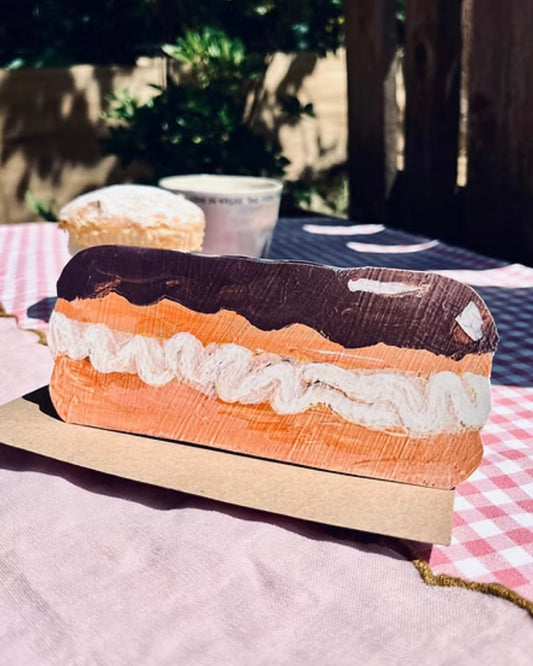 Shaped card with chocolate eclair illustration, standing on a brown kraft envelope, in an outdoor picnic table setting.
