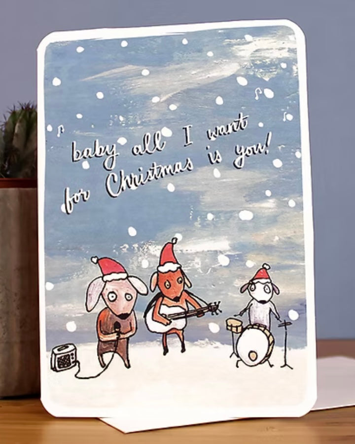 Card with cartoon dogs playing instruments against a snowy background, with the text ‘Baby all I want for Christmas is you’.