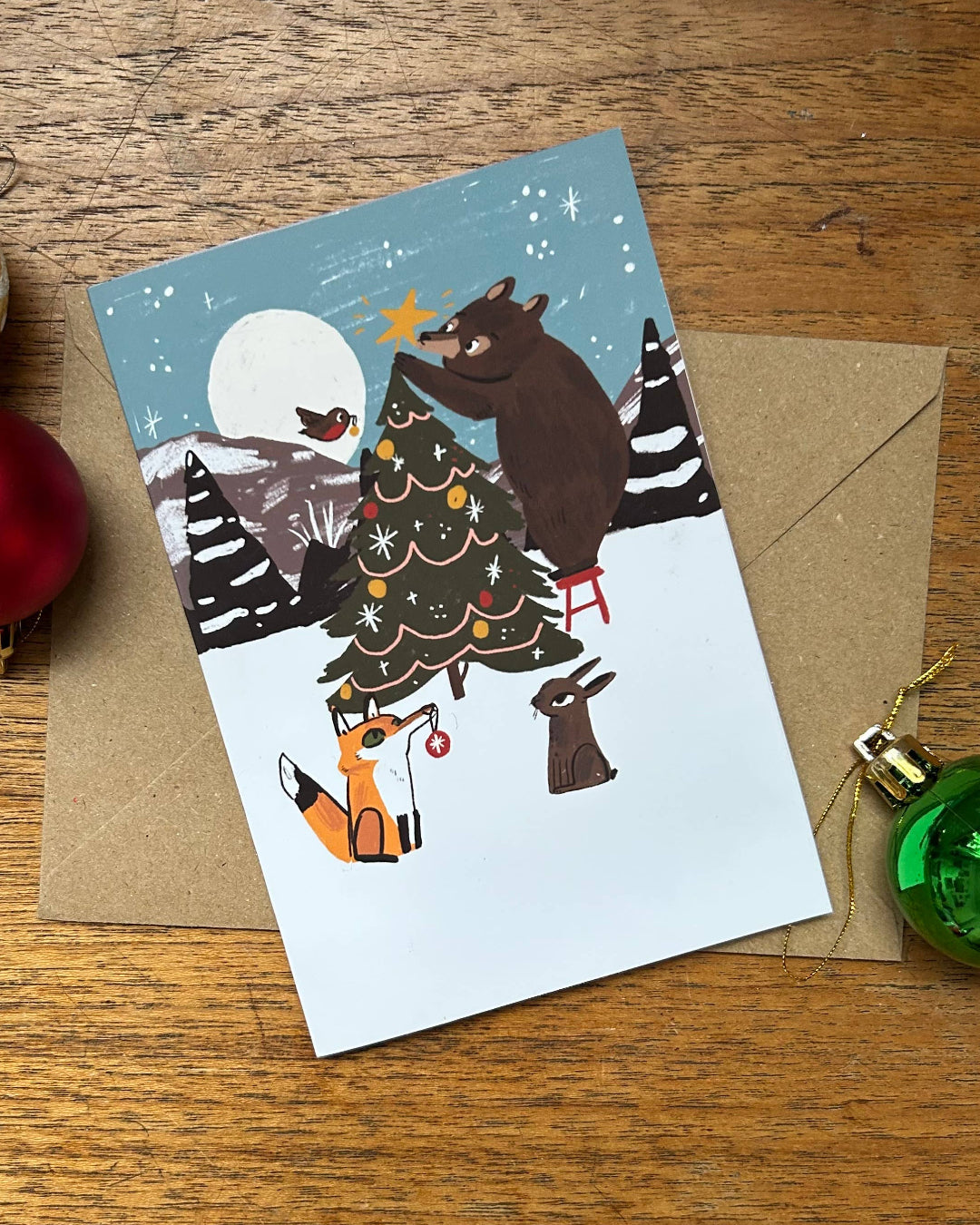 Christmas card with bears and a tree on a wooden surface with ornaments.