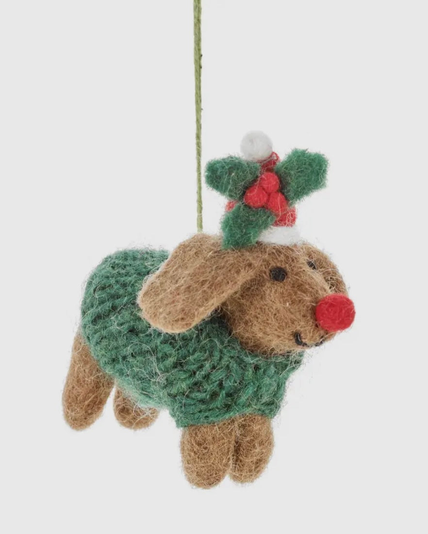 Decorative dog ornament wearing a green sweater with a red nose and holly leaves on a white background