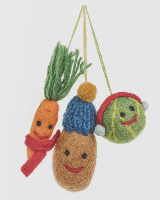 Decorative ornaments shaped like a carrot, potato, and brussel sprout with faces on a white background.