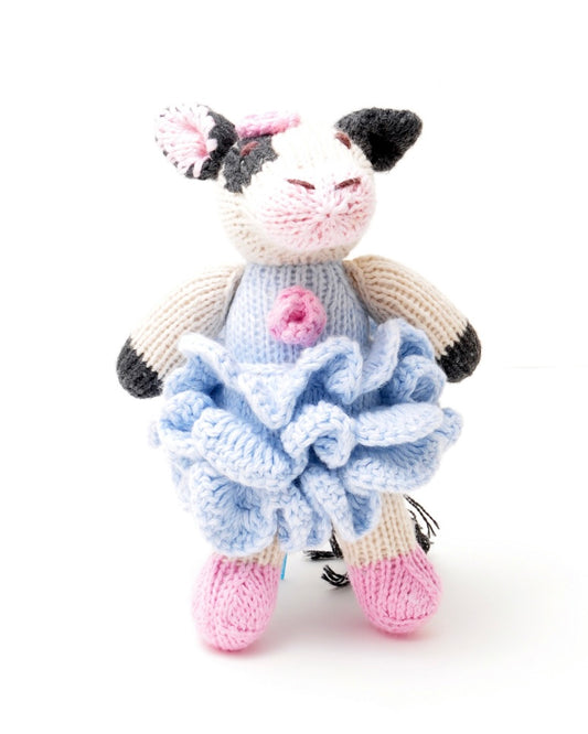 Knitted cow toy with a blue frilly dress, on a white background.