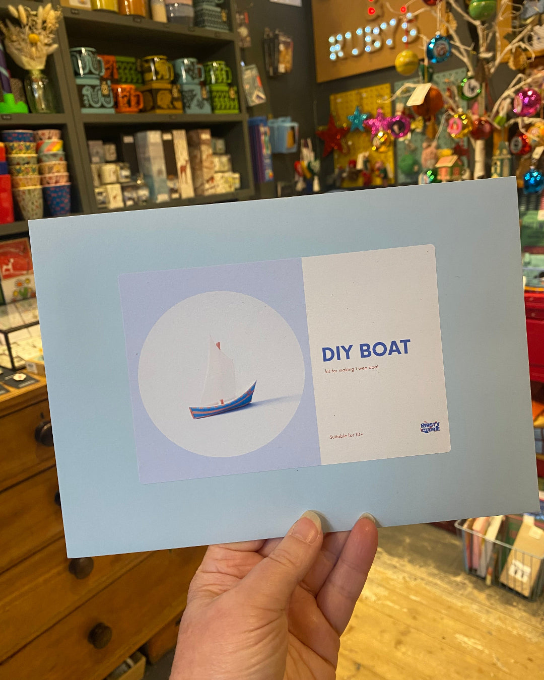 Hand holding a DIY boat kit with a store in the background