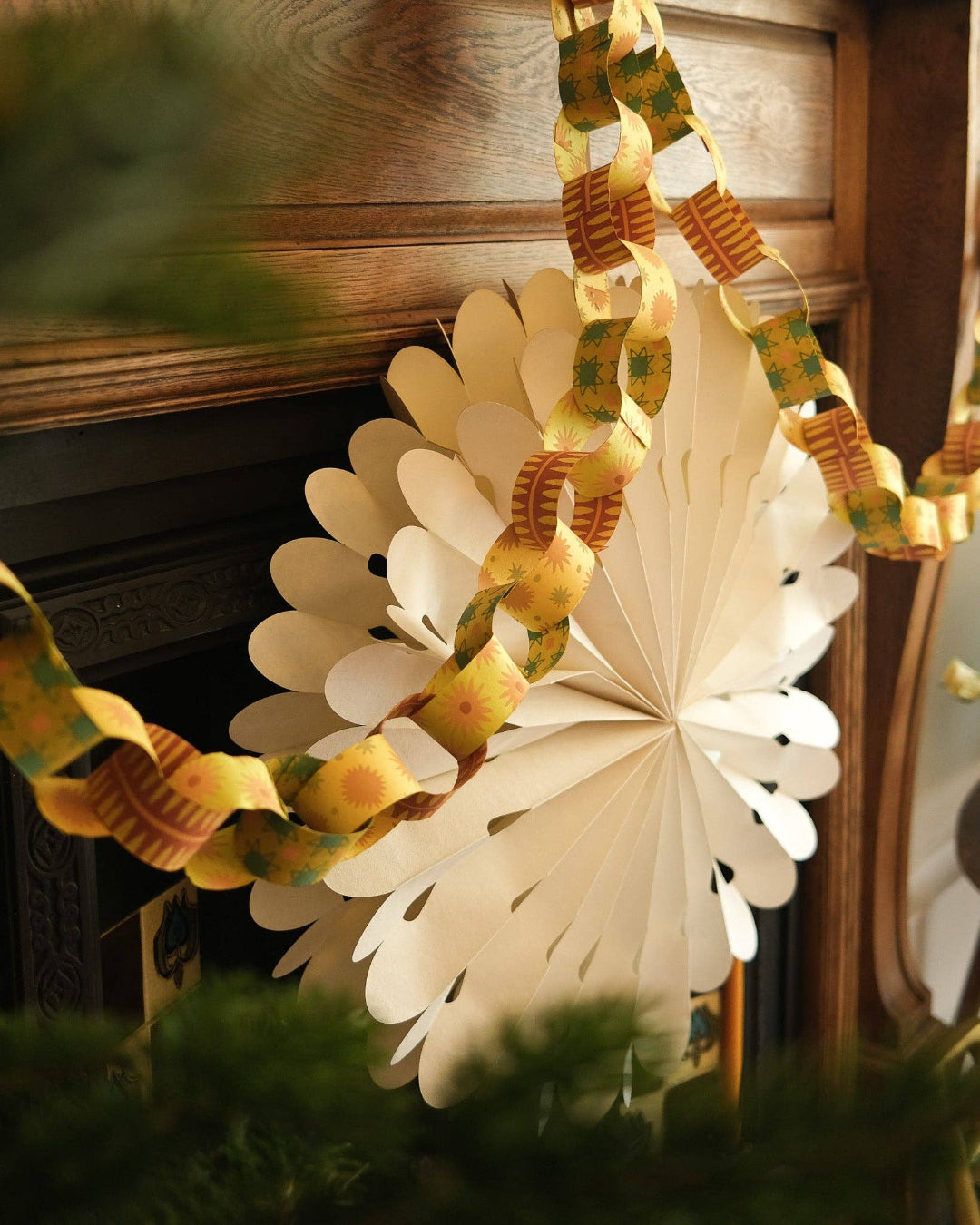 Decorative paper chain with floral design and a large white decoration hanging against a wooden wall.