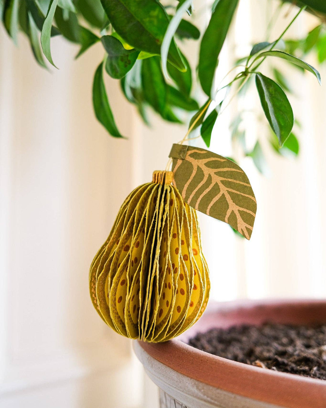 Decorative paper fruit hanging from a plant with a blurred background