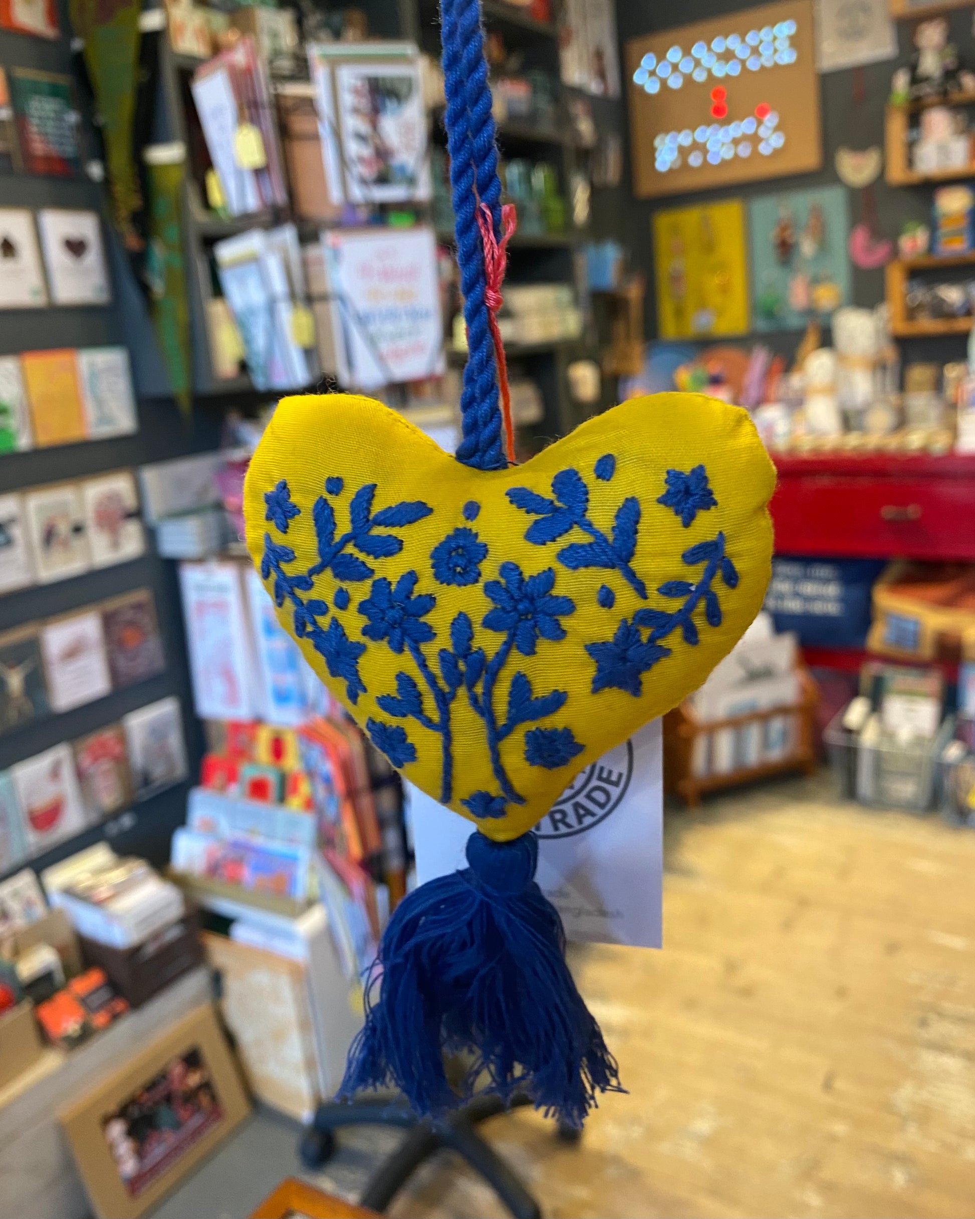 Yellow heart-shaped ornament with blue floral patterns and tassle in a store setting