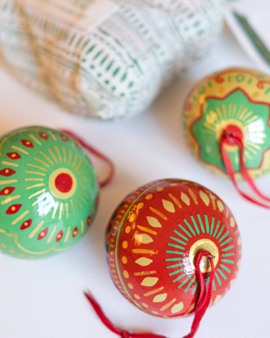 Decorative festive papier mache baubles with intricate designs with hanging loops on a white surface.