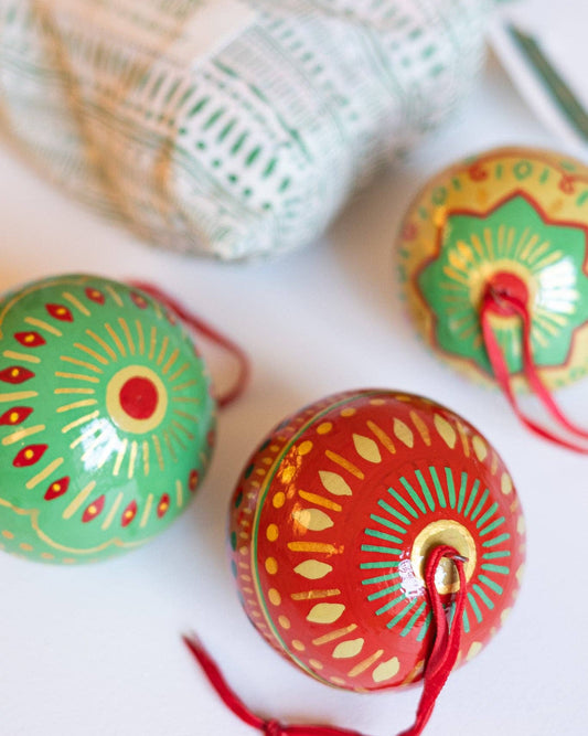 Decorative festive papier mache baubles with intricate designs with hanging loops on a white surface.