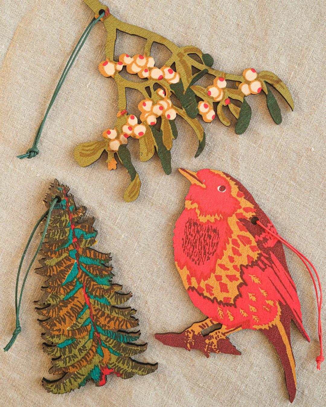 Decorative Christmas ornaments including a bird, tree, and mistletoe on a textured beige background.