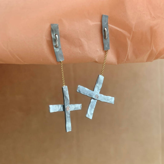 Pair of silver cross-shaped earrings on a brown background