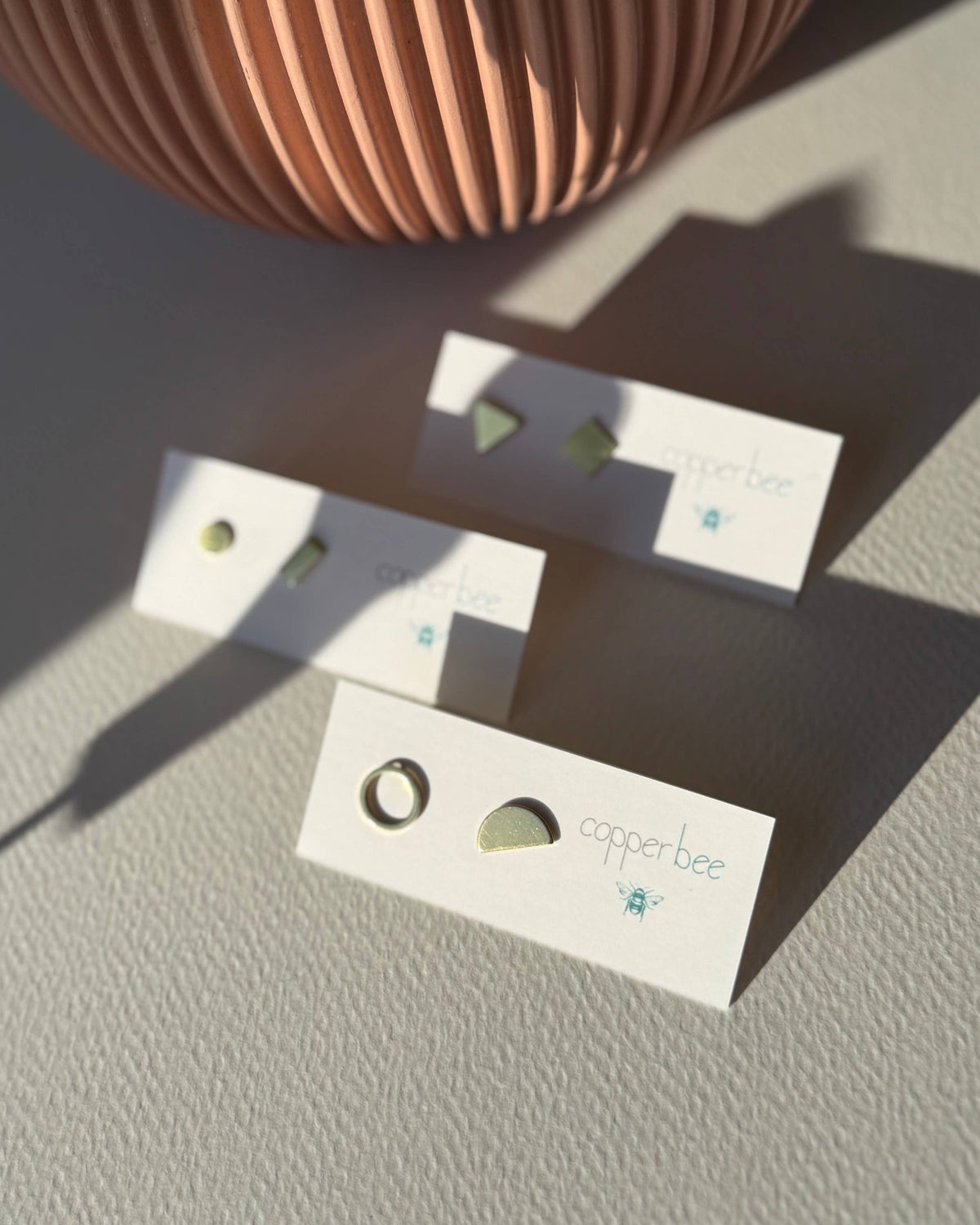 Three pairs of earrings on display cards with a plant in the background