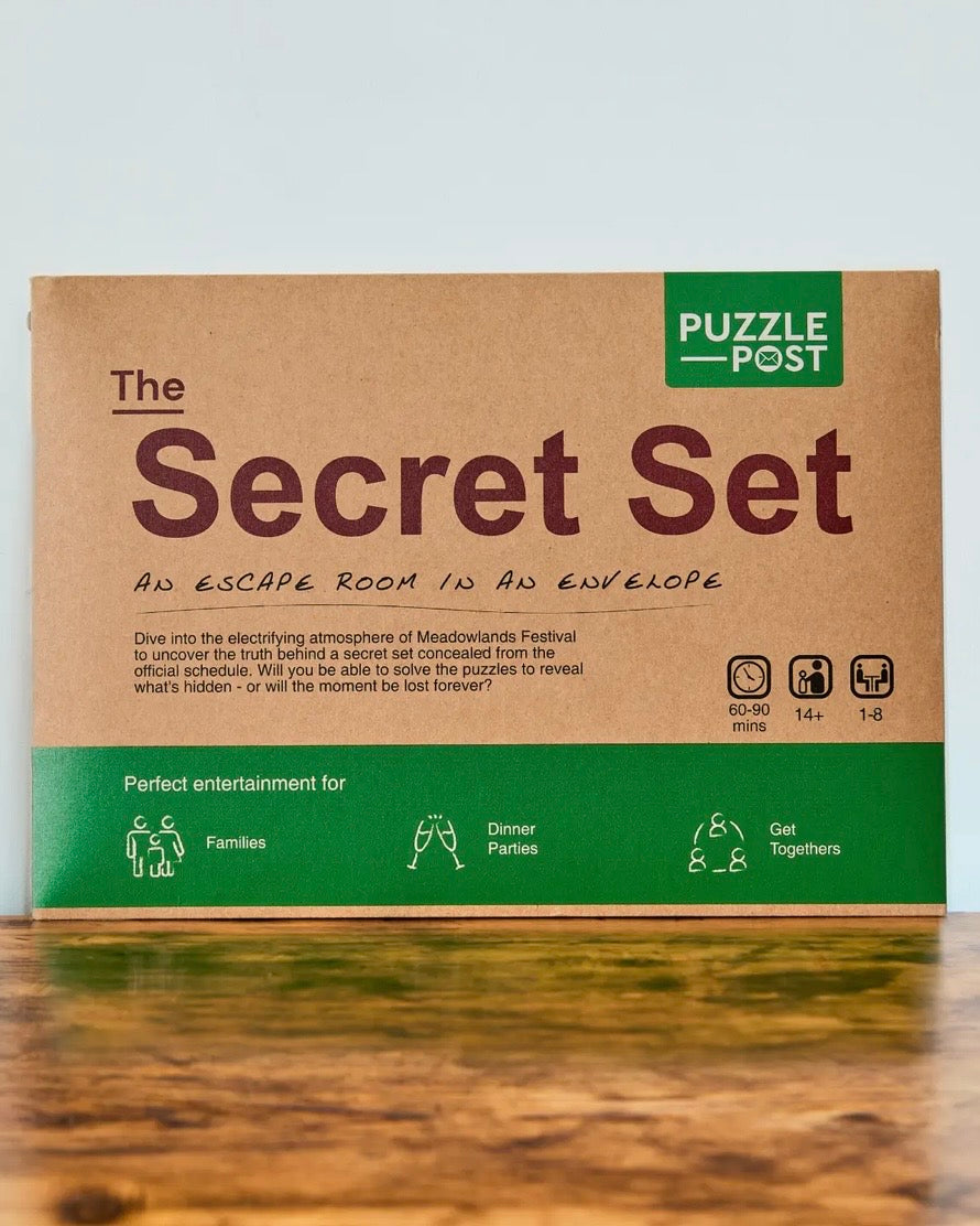 The Secret Set escape room puzzle envelope box by Puzzle Post, featuring a brown kraft paper design with green accents and text, displayed on a wooden surface against a light grey background.