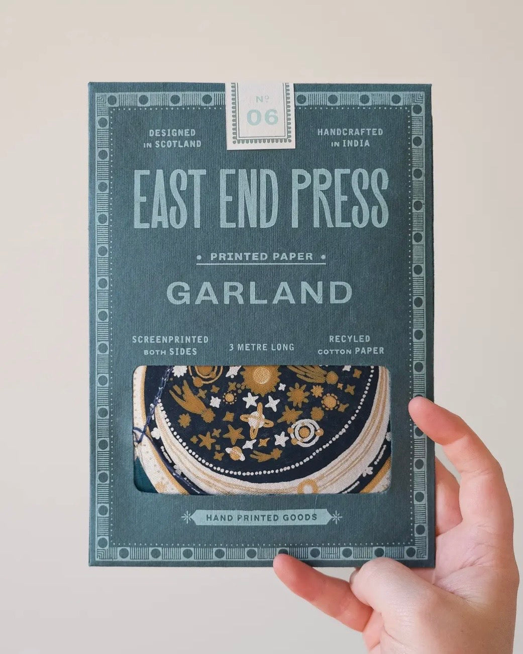 Hand holding a package of East End Press Garland printed paper against a plain background
